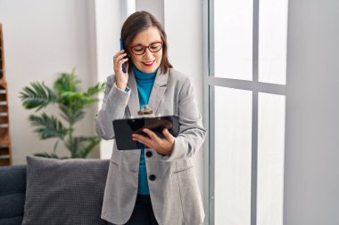 Middle age woman psychologist talking on the smartphone reading document at psychology center