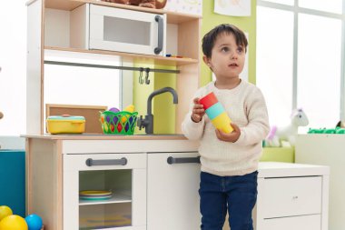 Adorable hispanic boy playing with play kitchen standing at kindergarten