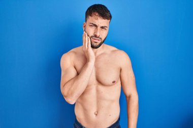 Handsome hispanic man standing shirtless touching mouth with hand with painful expression because of toothache or dental illness on teeth. dentist 