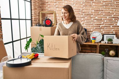 Young caucasian woman smiling confident holding kitchen package at new home