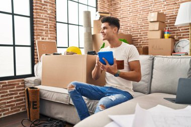 Yeni evindeki koltukta oturan dokunmatik ped kullanan İspanyol genç adam.