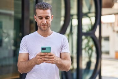 Young caucasian man using smartphone with relaxed expression at street