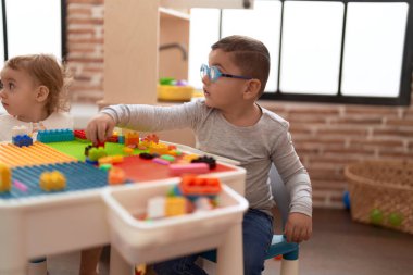 Anaokulundaki masada oturan sevimli kız ve oğlan inşaat bloğu parçalarıyla oynuyorlar.