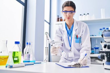 Young beautiful hispanic woman scientist writing report working at laboratory