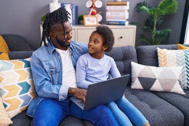 Father and daughter using laptop sitting on sofa at home