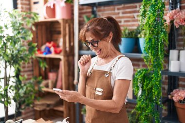Middle age woman florist smiling confident using smartphone at flower shop