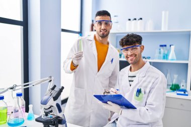 Two man scientists holding test tube write on clipboard working at laboratory