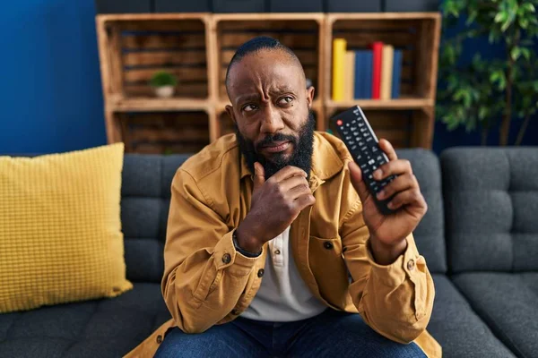 African American Man Holding Television Remote Control Serious Face Thinking — Photo