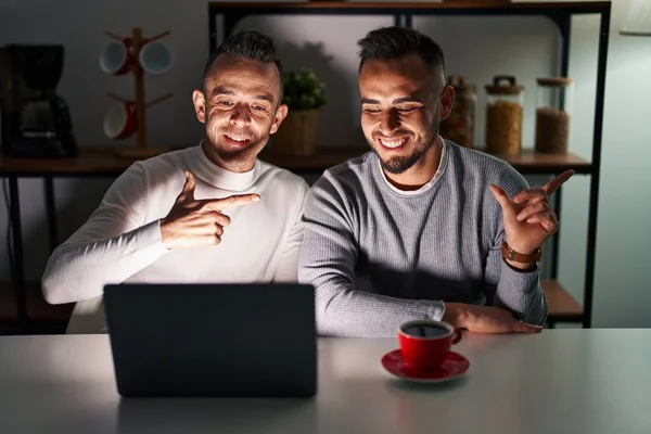 Homosexual couple using computer laptop cheerful with a smile on face pointing with hand and finger up to the side with happy and natural expression