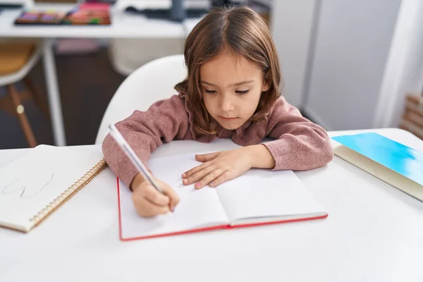 Adorable Hispanic Girl Student Sitting Table Writing Notebook Classroom — Fotografia de Stock