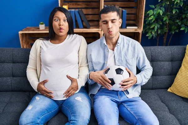 Young Hispanic Couple Expecting Baby Sitting Sofa Holding Ball Tummy — ストック写真