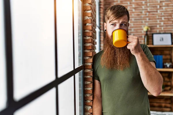 Young redhead man drinking coffee at home