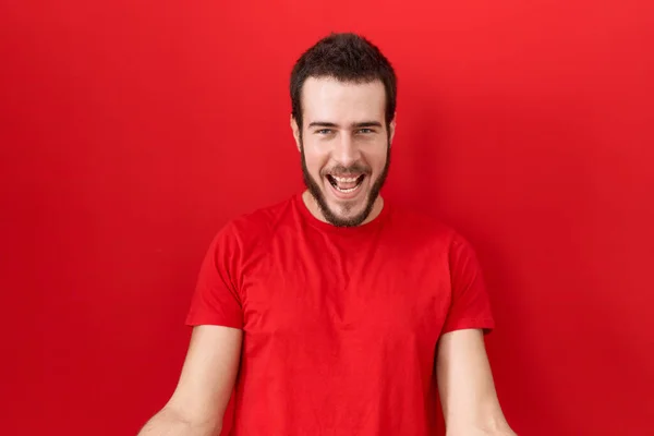 優しい歓迎 正と自信を持って挨拶として腕を開いて陽気に笑顔カジュアルな赤いTシャツを着て若いヒスパニック系の男 — ストック写真