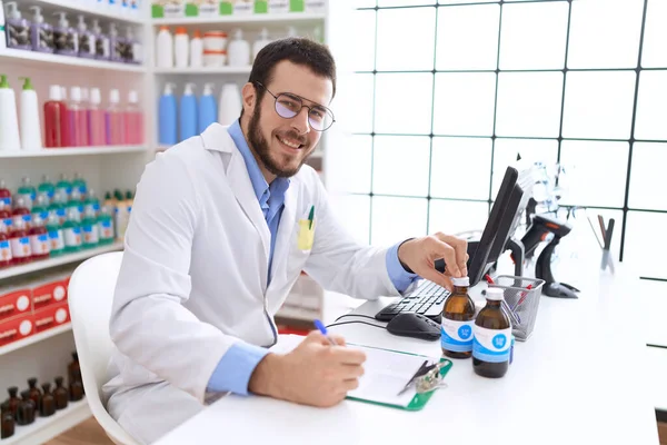 Young Hispanic Man Pharmacist Holding Medication Bottle Writing Document Pharmacy — Stock Photo, Image