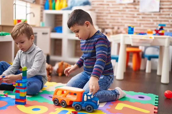 幼稚園の床に座っている建設ブロックやトラックのおもちゃで遊んでいる2人の子供 — ストック写真