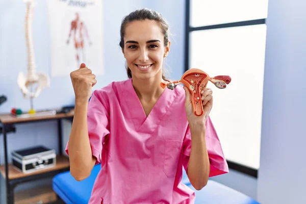 Young hispanic woman holding model of female genital organ at rehabilitation clinic screaming proud, celebrating victory and success very excited with raised arms