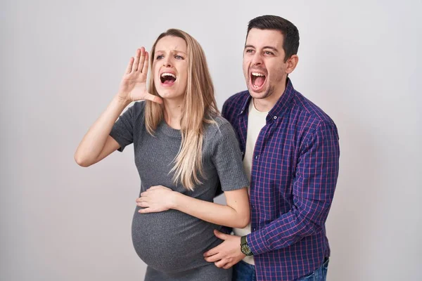 白い背景の上に立つ赤ん坊を期待して大声で叫び 口の上で手で横に大声で叫ぶカップル コミュニケーションの概念 — ストック写真