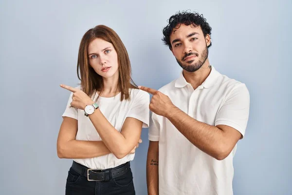 年轻夫妇穿着休闲装站在一起 手指头指向广告的侧面 严肃而沉着 — 图库照片