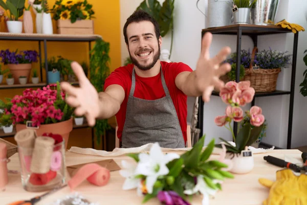 stock image Young hispanic man working at florist shop looking at the camera smiling with open arms for hug. cheerful expression embracing happiness. 