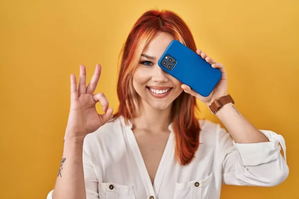 Young Caucasian Woman Covering Eye Smartphone Doing Sign Fingers Smiling — 스톡 사진