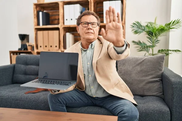 Senior psychiatrist man working at consultation office with online session with open hand doing stop sign with serious and confident expression, defense gesture