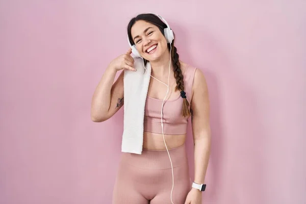 Young brunette woman wearing sportswear and headphones smiling doing phone gesture with hand and fingers like talking on the telephone. communicating concepts.
