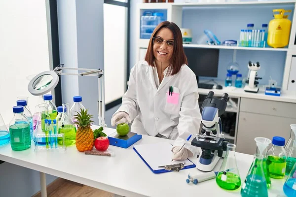 Young Beautiful Hispanic Woman Scientist Weighing Apple Writing Document Laboratory — Stockfoto