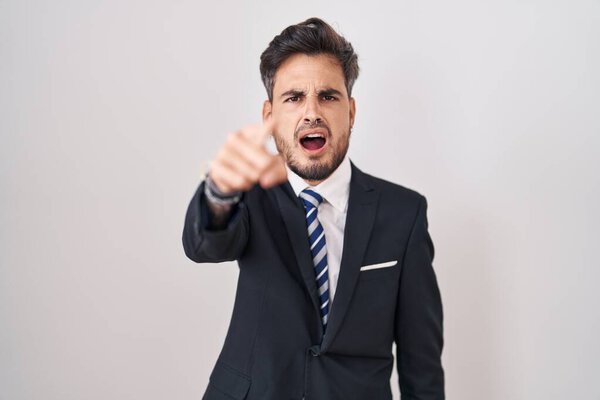 Young hispanic man with tattoos wearing business suit and tie pointing displeased and frustrated to the camera, angry and furious with you 
