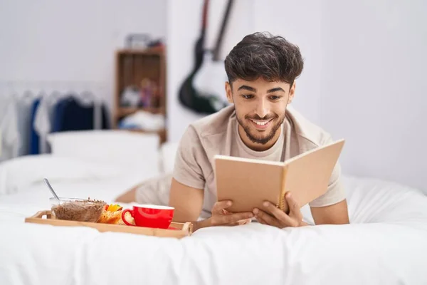 Young arab man reading book having breakfast at bedroom