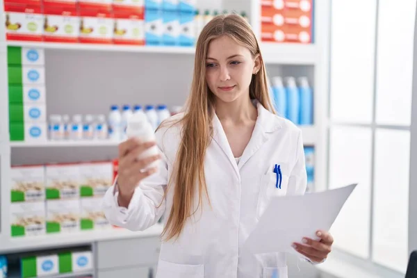 Young Caucasian Woman Pharmacist Holding Pills Bottle Reading Prescription Pharmacy — Stockfoto