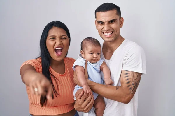 Young hispanic couple with baby standing together over isolated background pointing displeased and frustrated to the camera, angry and furious with you