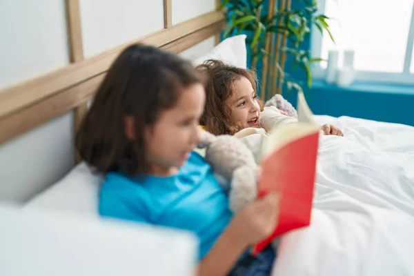 Two kids reading story book sitting on bed at bedroom