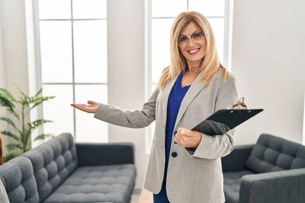 Middle age blonde woman psychologist smiling confident standing at clinic