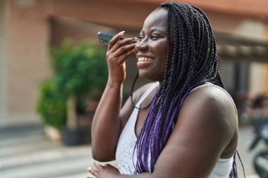 Afro-Amerikalı kadın gülümsüyor. Kafe terasındaki akıllı telefonun kendine güvenen sesli mesajını dinliyor.