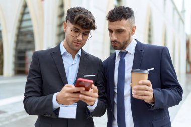 Two hispanic men business workers using smartphone drinking coffee at street