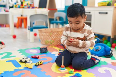 Anaokulunda yerde oturmuş halkalarla oynayan sevimli İspanyol çocuk.