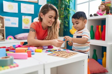 Teacher and toddler playing with maths puzzle game sitting on table at kindergarten
