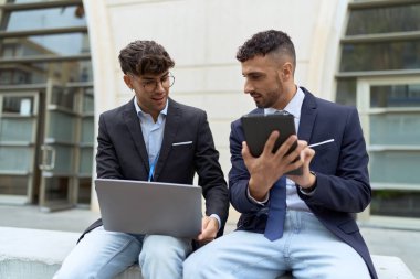 Two hispanic men business workers using touchpad and laptop working at street