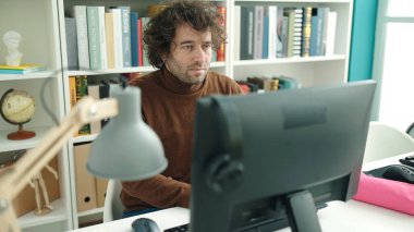 Young hispanic man student using computer studying at library university