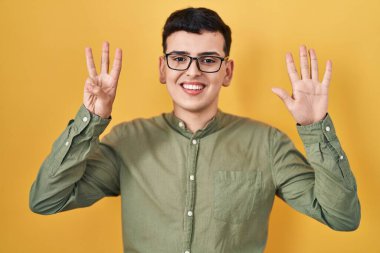Non binary person standing over yellow background showing and pointing up with fingers number eight while smiling confident and happy. 