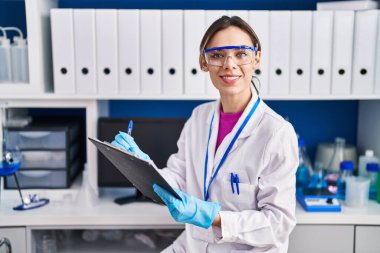 Young beautiful hispanic woman scientist writing report working at laboratory