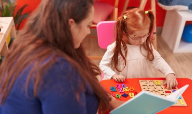 Teacher and student playing with maths puzzle game reading book at kindergarten