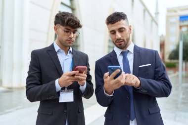 Two hispanic men business workers using smartphones at street
