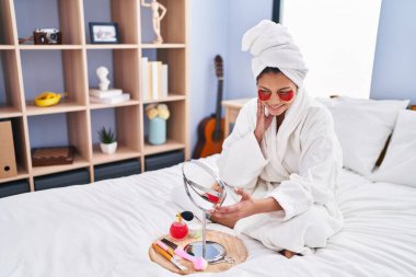 Genç Latin kadın, yatakta uzanmış, dolgun göz tedavisi görüyor.