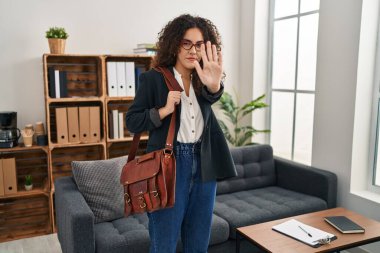 Young hispanic woman at consultation office with open hand doing stop sign with serious and confident expression, defense gesture 