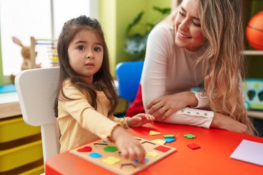 Teacher and toddler playing with maths puzzle game sitting on table at kindergarten