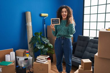 Elinde yeni ev yazısıyla tahtası olan genç İspanyol bir kadın bir fikir veya soruyla gülümsüyor ve mutlu bir yüzle işaret ediyor. 