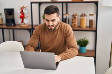 Evdeki masada dizüstü bilgisayar kullanan genç bir İspanyol.