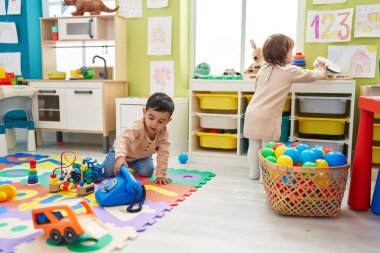 Anaokulunda yerde oturan iki çocuk telefon oyuncağıyla oynuyor.