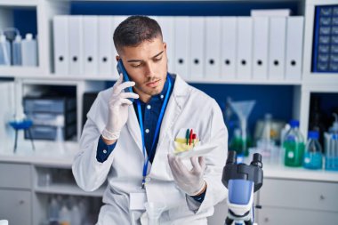 Young hispanic man scientist talking on the smartphone at laboratory